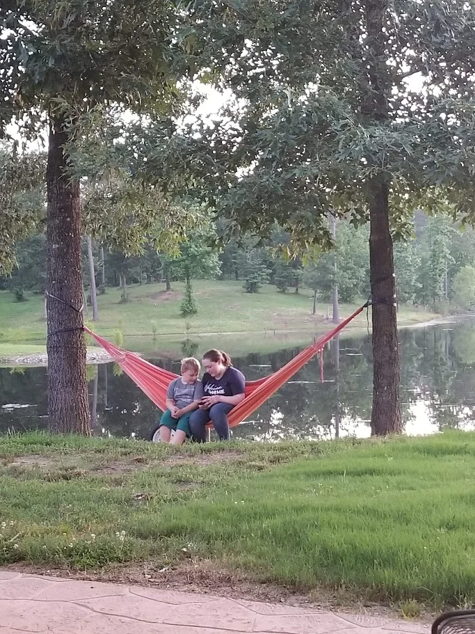 Family relaxing together in a hammock beside the pond